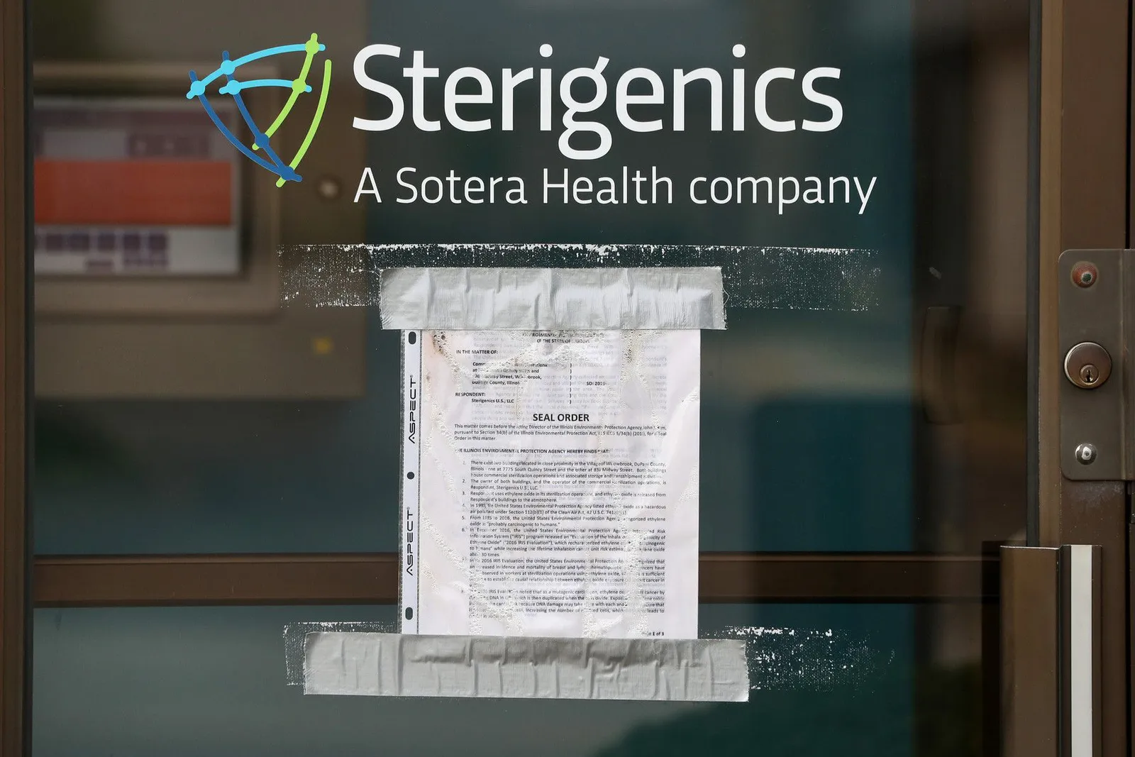 A paper denoting a seal order is taped to a glass door that says "Stergenics, A Sotera Health company."