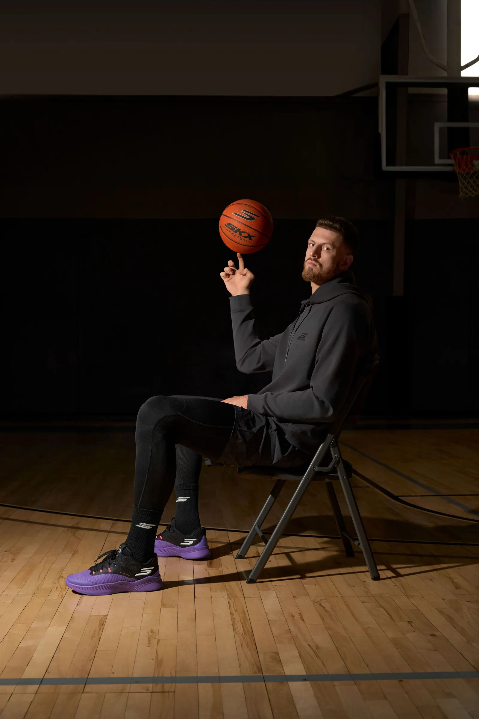 Isaiah Hartenstein sits in a chair in a gym, balancing a basketball on a finger.