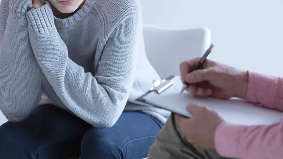 A young woman wrings her hands during a session with her psychotherapist.