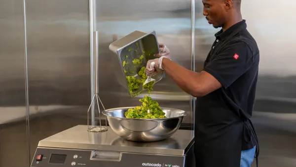 A man in a Chipotle uniform removes processed avocado from tray.