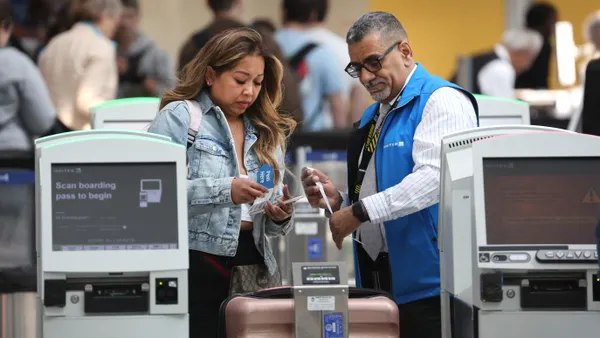 An employee aids a customer in attaching a tag to their luggage.
