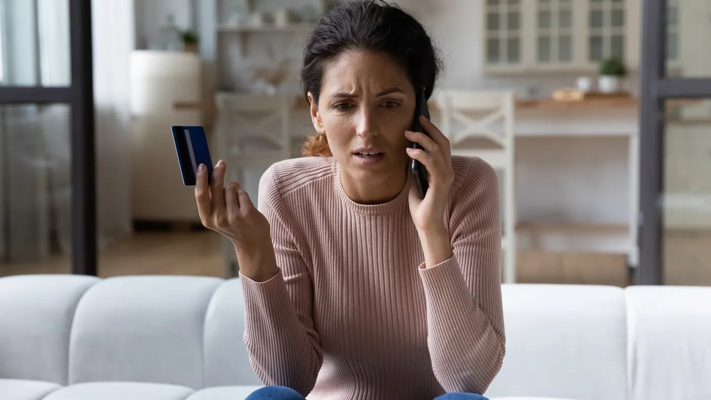 A woman is on the phone with customer service and holds her credit card.