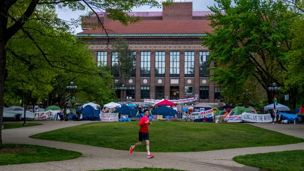 A person runs on the sidewalk past a protest encampment on the campus of the University of Michigan.