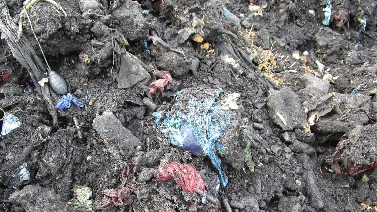 A pile of improperly incinerated trash containing ash and remnants of still visible biohazard bags, among other items.