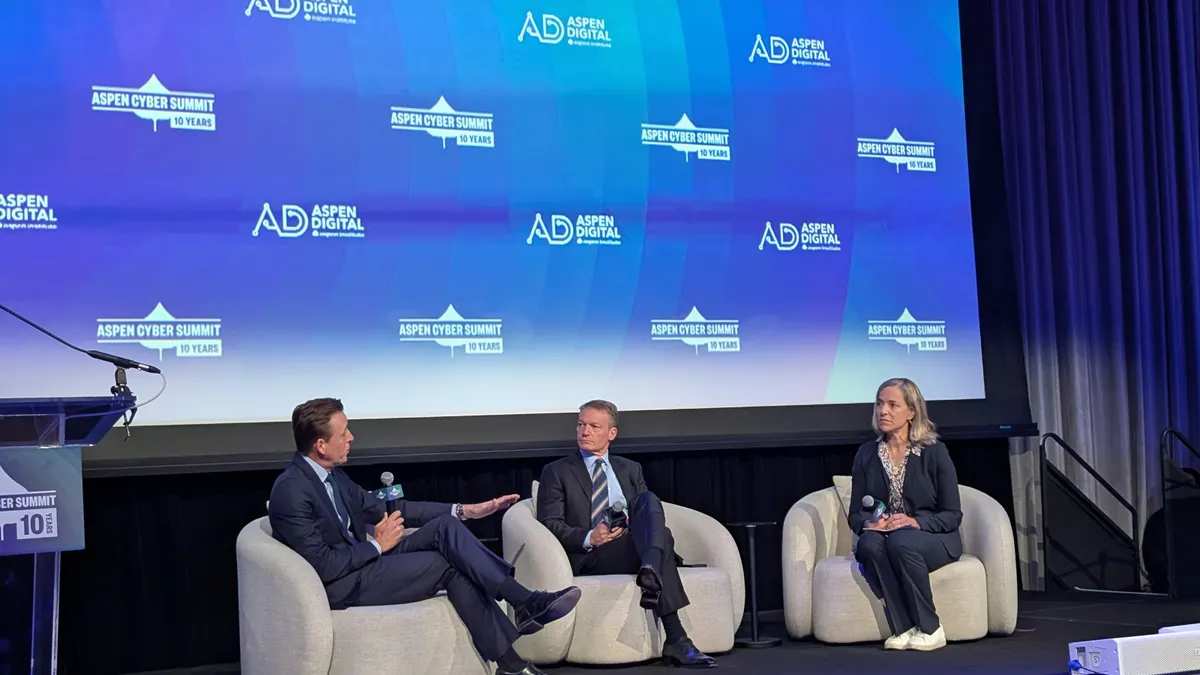 Two men and a woman sit in chairs on a stage in front of a screen showing the logos of the Aspen Cyber Summit and Aspen Digital