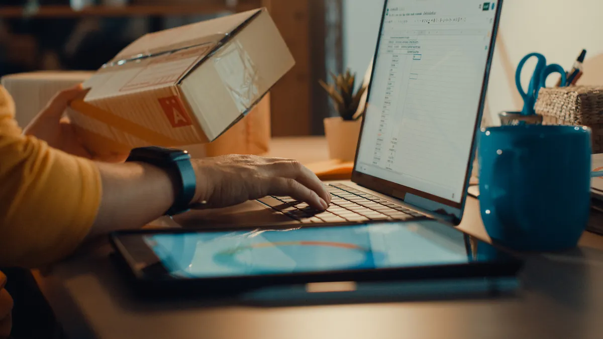 Person on laptop and holding brown box