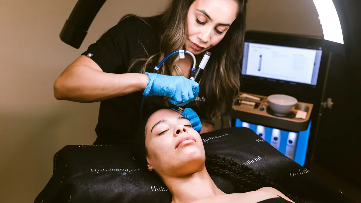 An esthetician using the Hydrafacial device on a client.