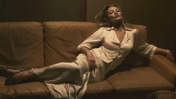 A person in a cream satin suit lounges on a couch