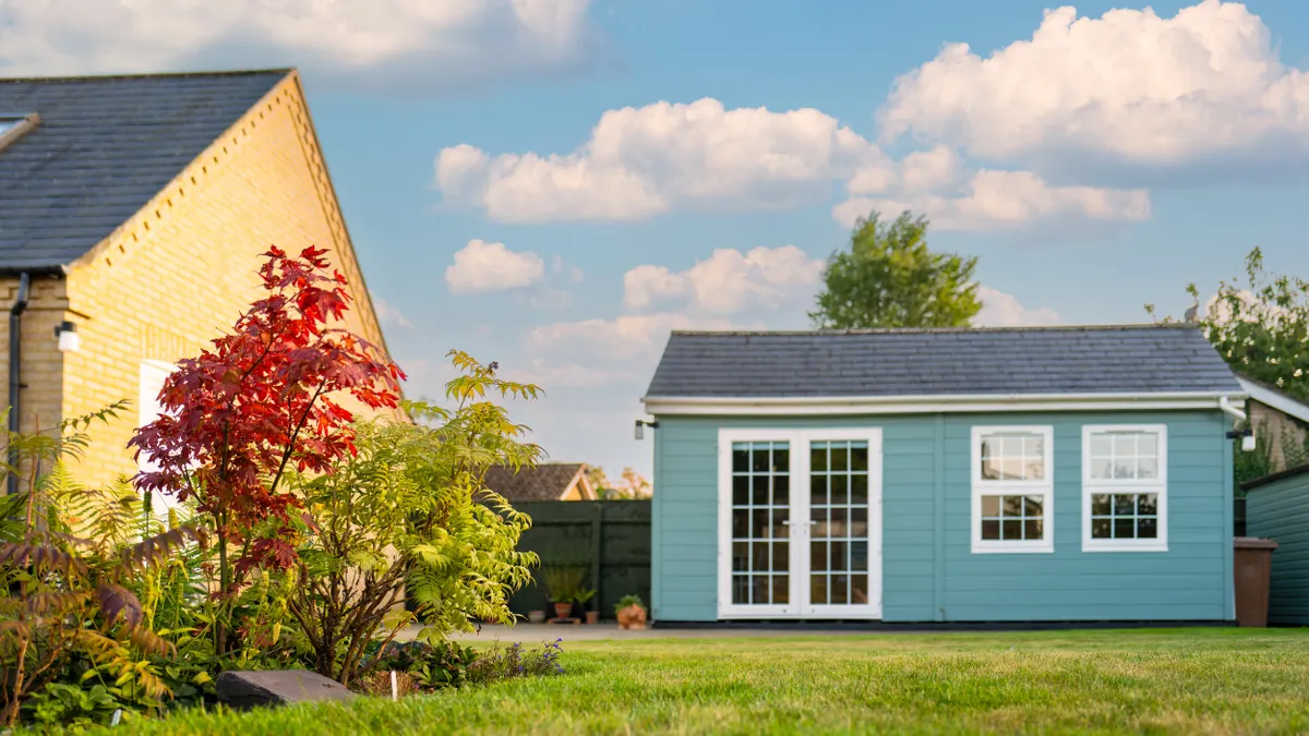 A small blue house sits next to a larger yellow house in a  yard.