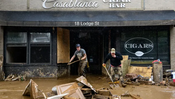 Building debris sits in mud outside a building that reads "Casablanca Cigar Bar 18 Lodge St." Two people carry items out of the building.