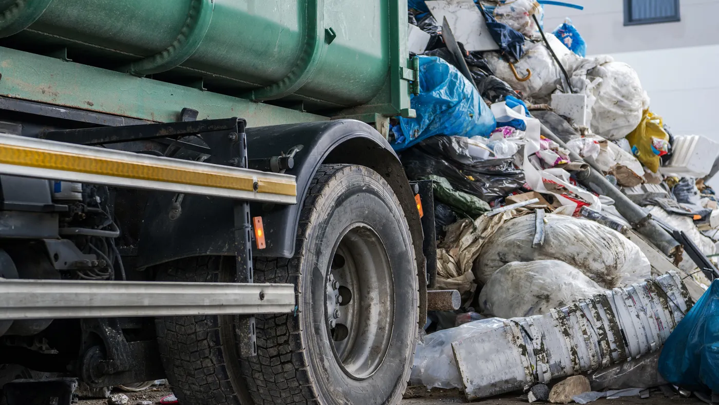 Wheel of trash truck next to pile of garbage and recycling