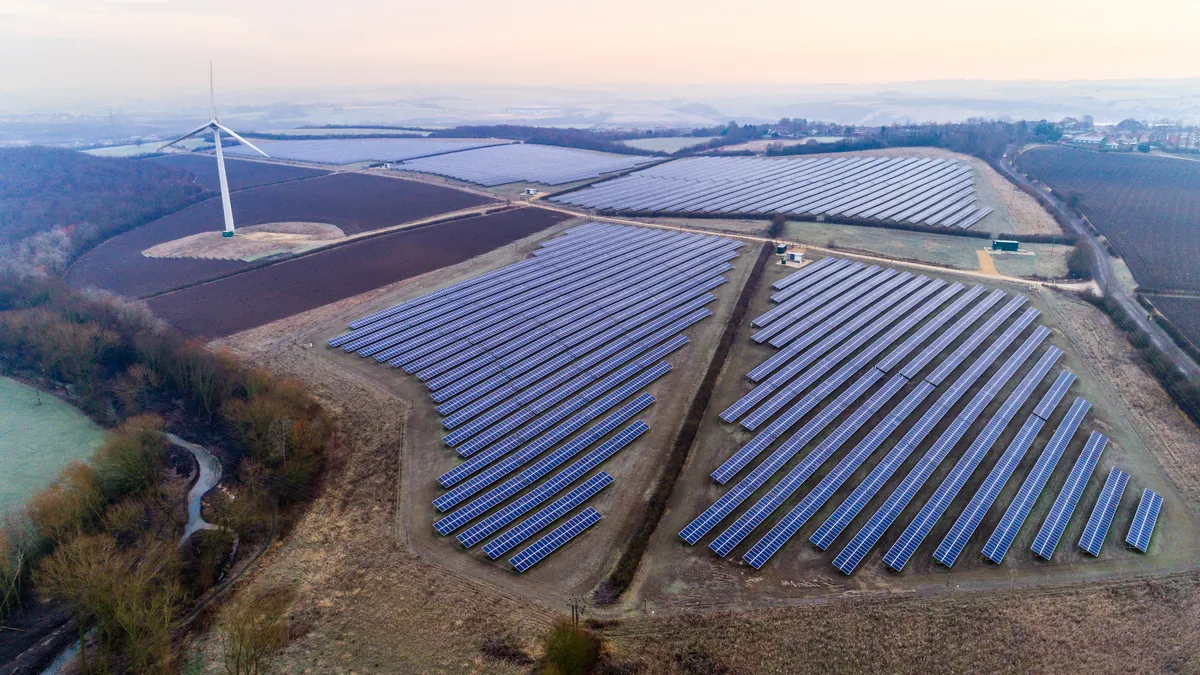 A wind turbine stands next to a solar farm.