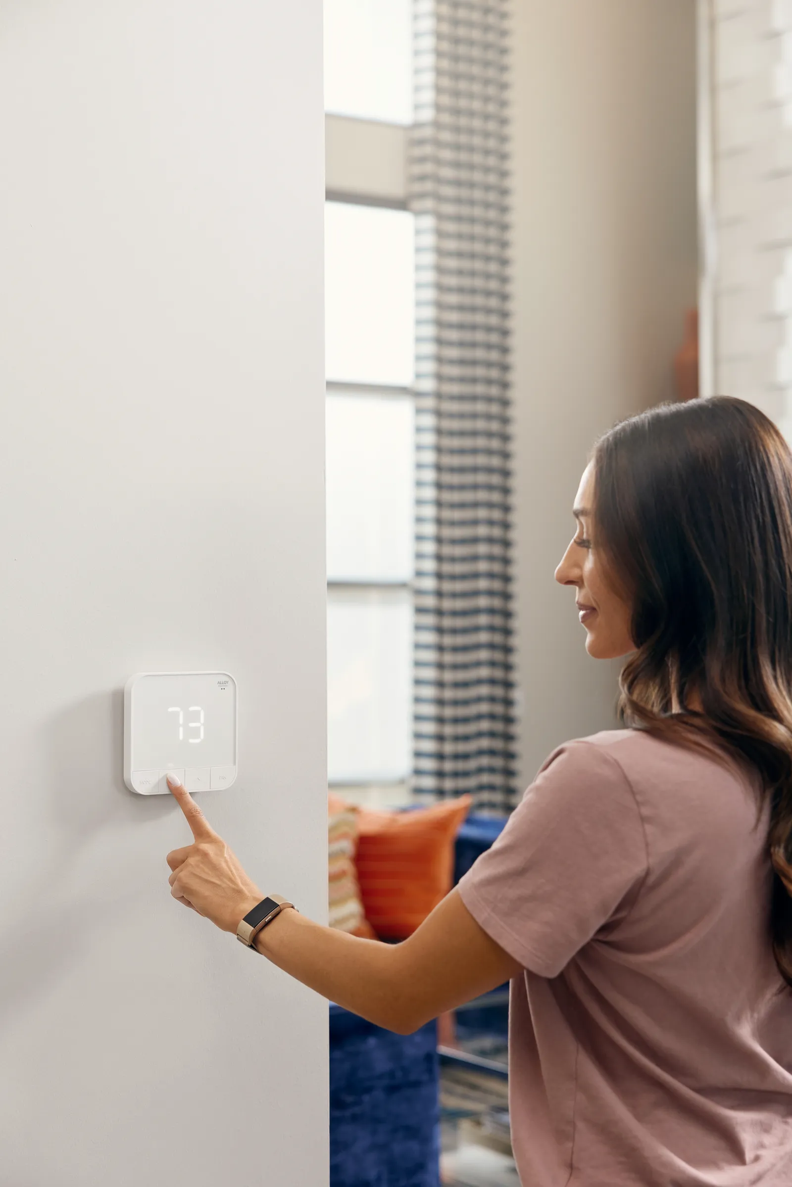 A person uses a smart thermostat on a wall.