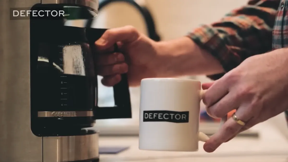 A person holds a Defector Media branded coffee mug
