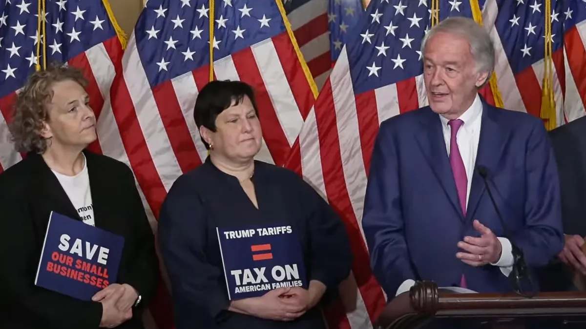People gathered around a microphone, with U.S. flags behind them.