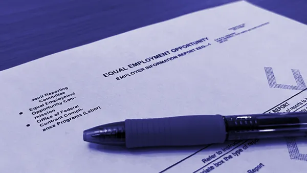 A printed copy of the EEOC's EEO-1 reporting form and a pen on top of a wooden table