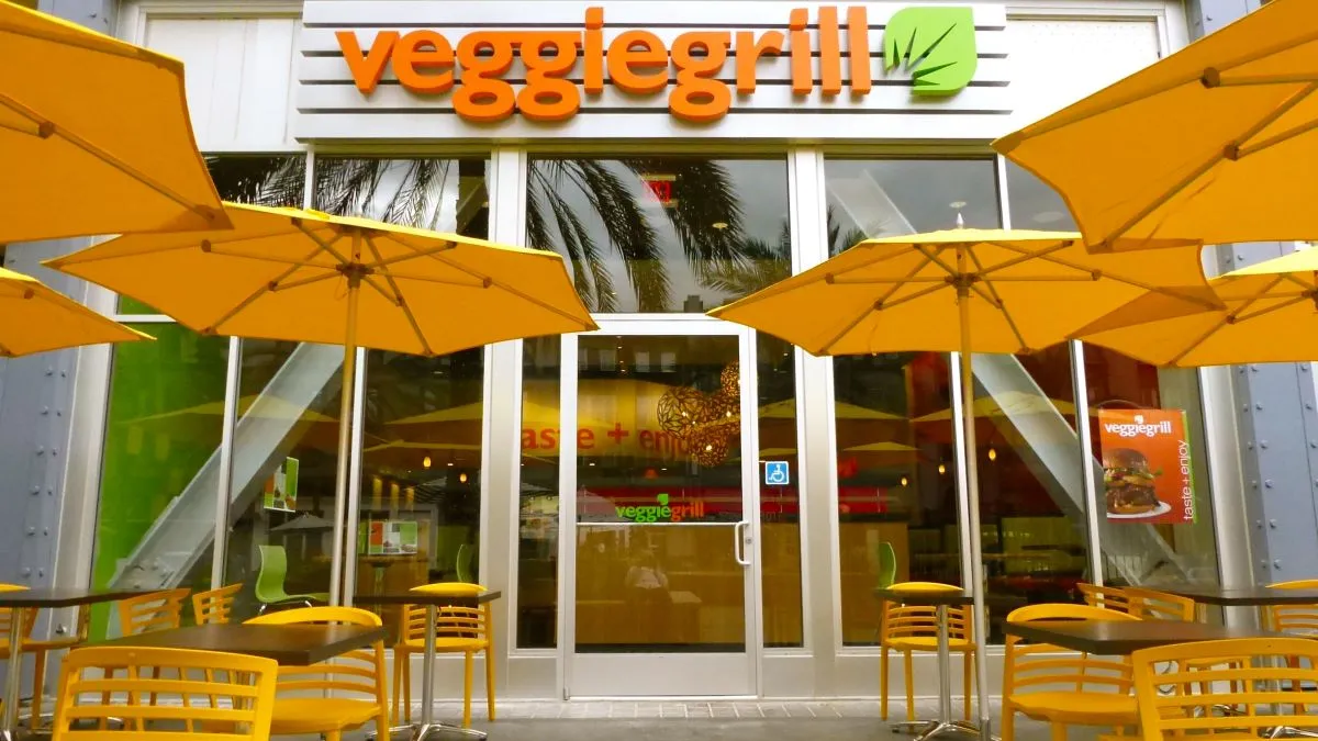 An image of a Veggie Grill restaurant with tables and umbrellas outside.