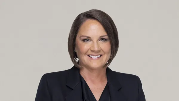 A person with bobbed hair wearing a dark jacket smiles slightly.