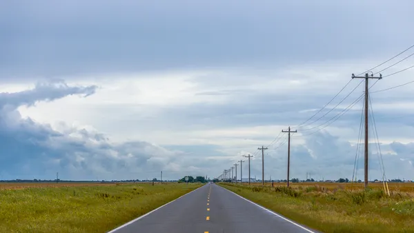 A vacant road with a dotted passing line for traffic next to telephone poles and open fields.