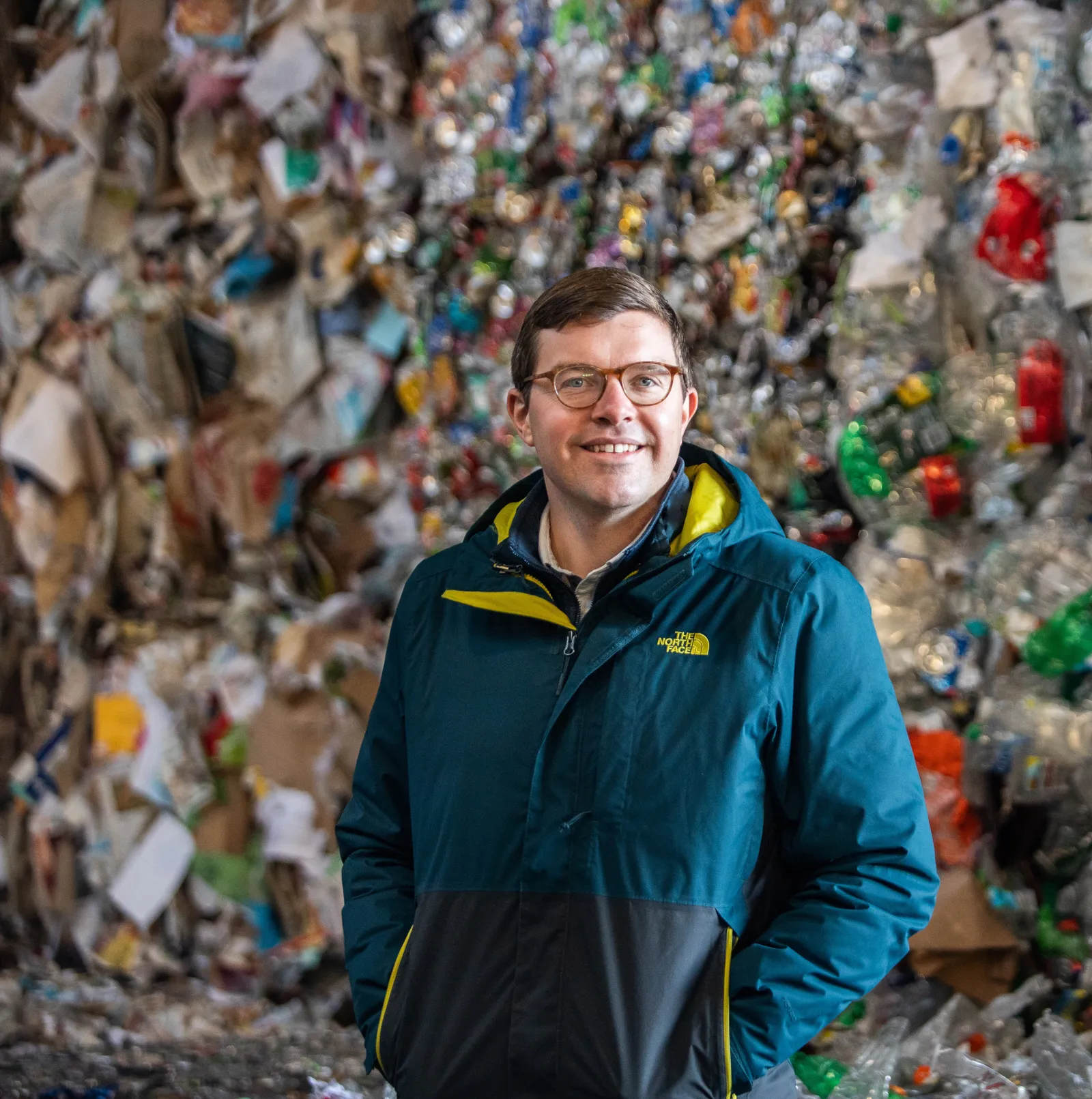 Person in jacket and glasses standing in front of baled recyclables