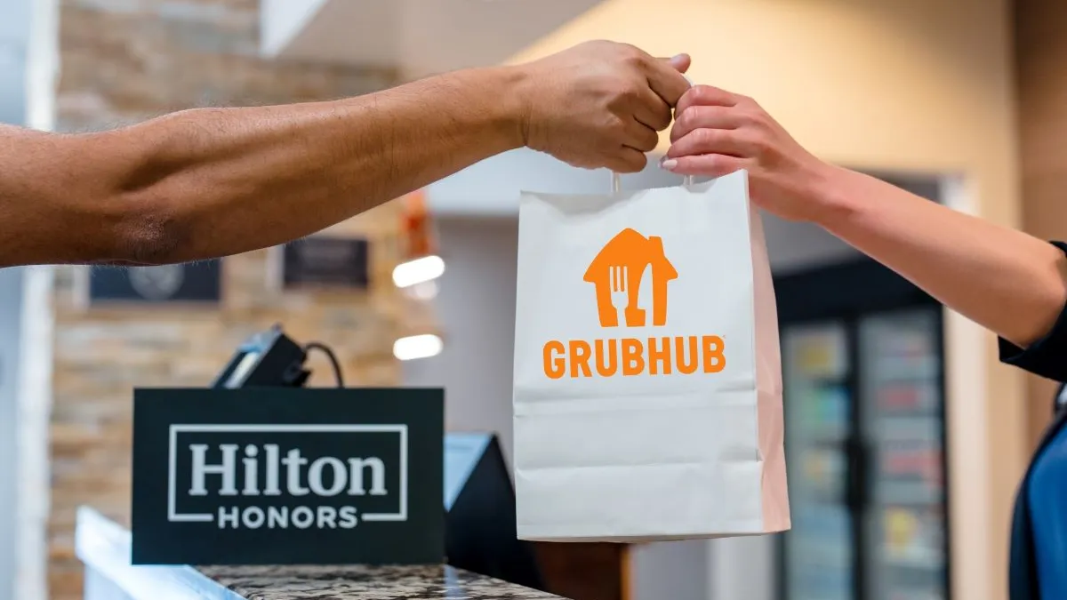 An image of an arm reaching to take a bag with a Grubhub logo on it.