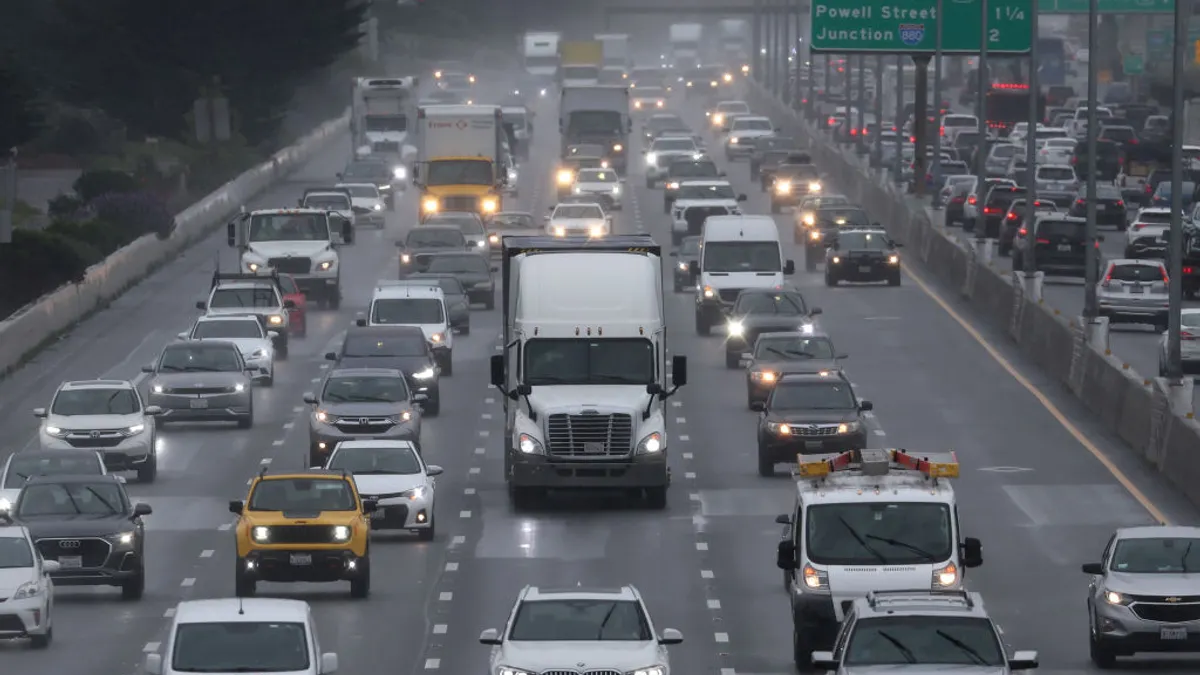 Several cars and trucks drive through a freeway on a semi-foggy day.
