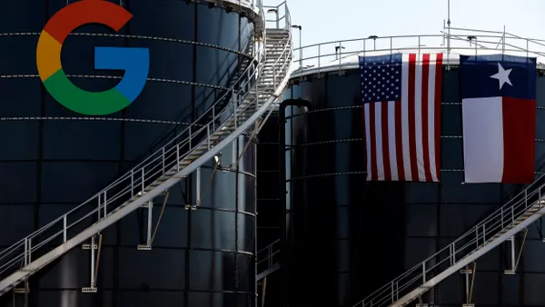 A round building with a large G and more buildings behind a U.S. and a Texas flag.