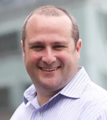 Man smiling with blurred building in the background.