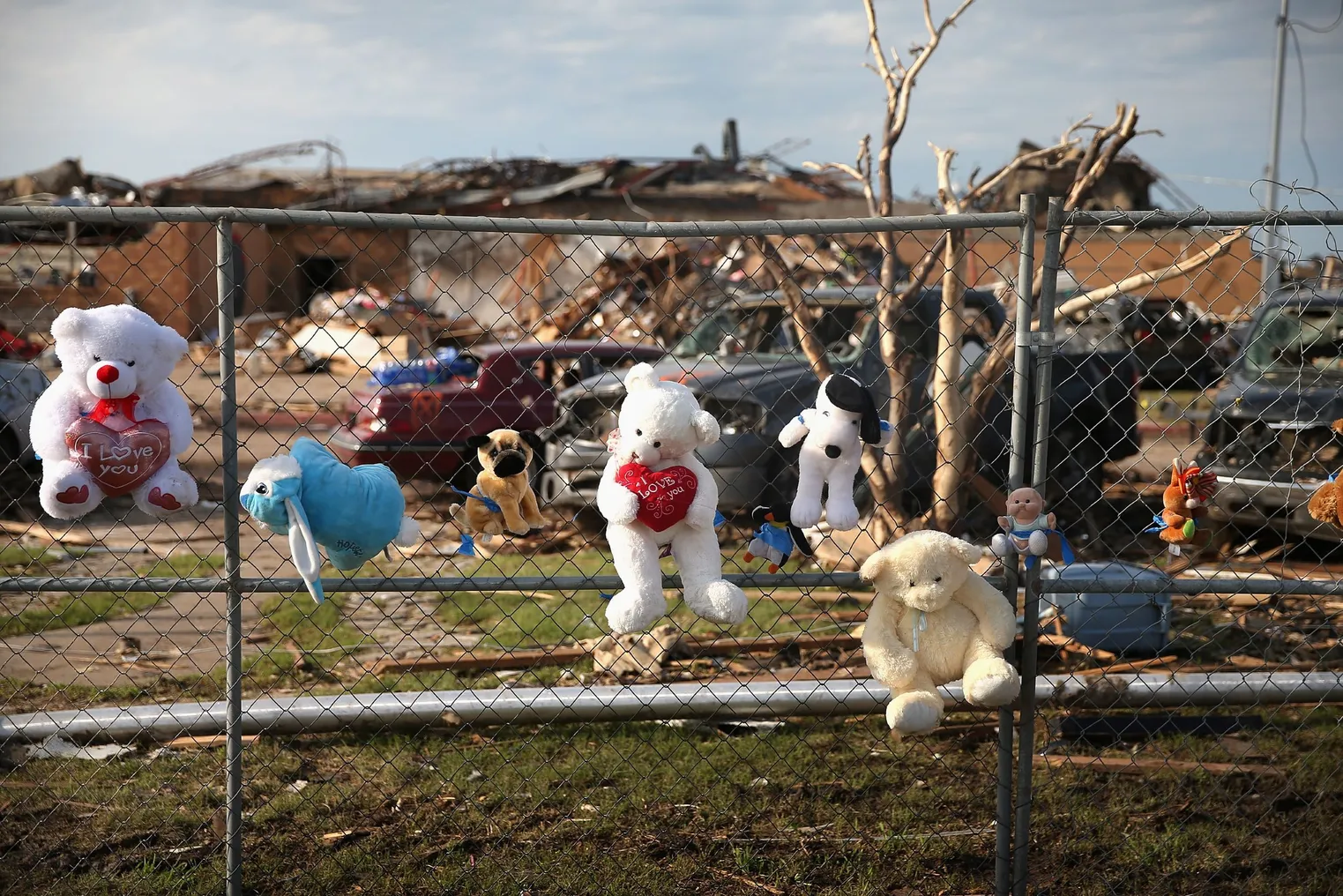 A row of stuffed animals are attached to a fence in front of the rubble left behind from a lethal tornado that hit an elementary school on May 20, 2013.