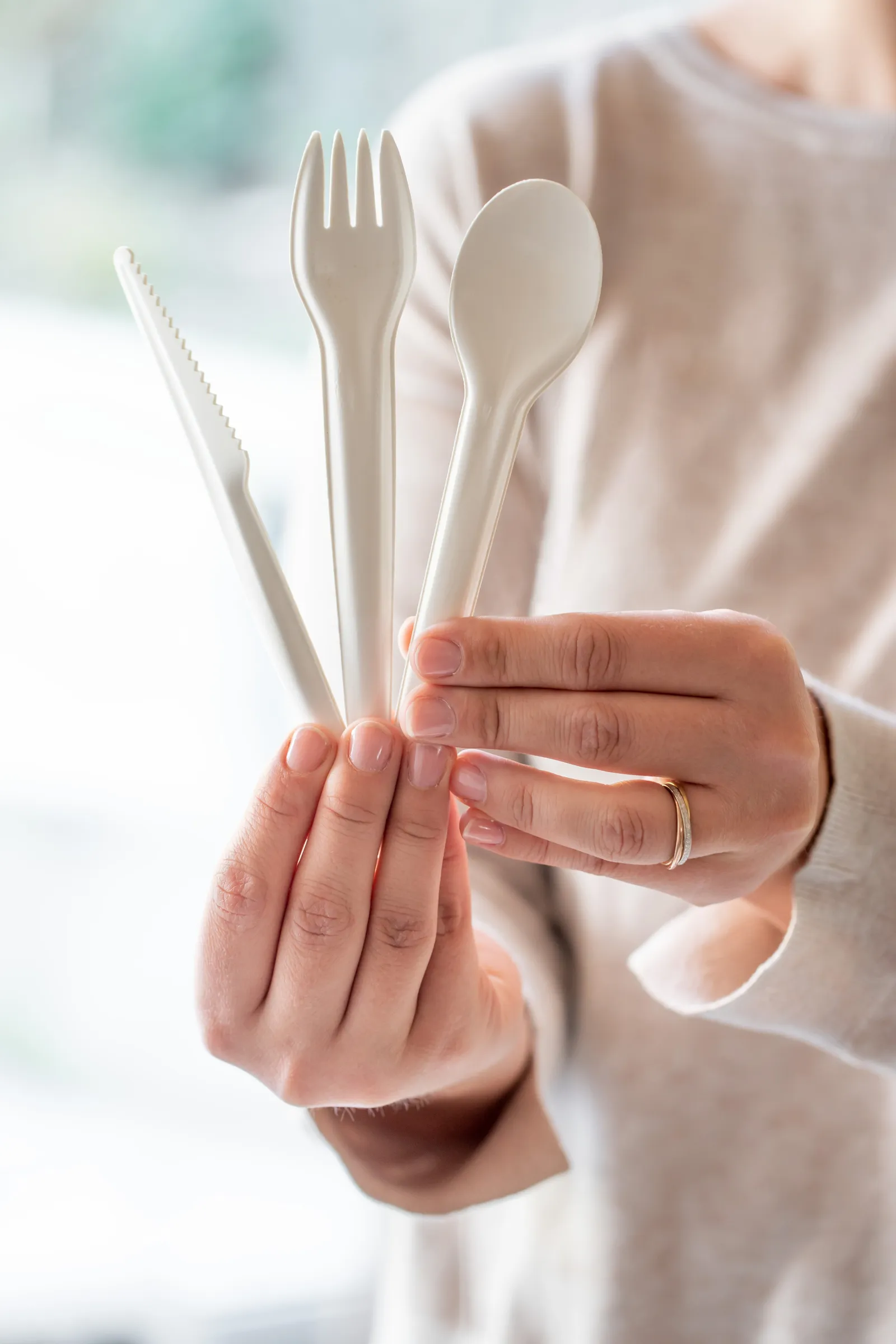 A person holding a knife, fork and spoon made from paper.