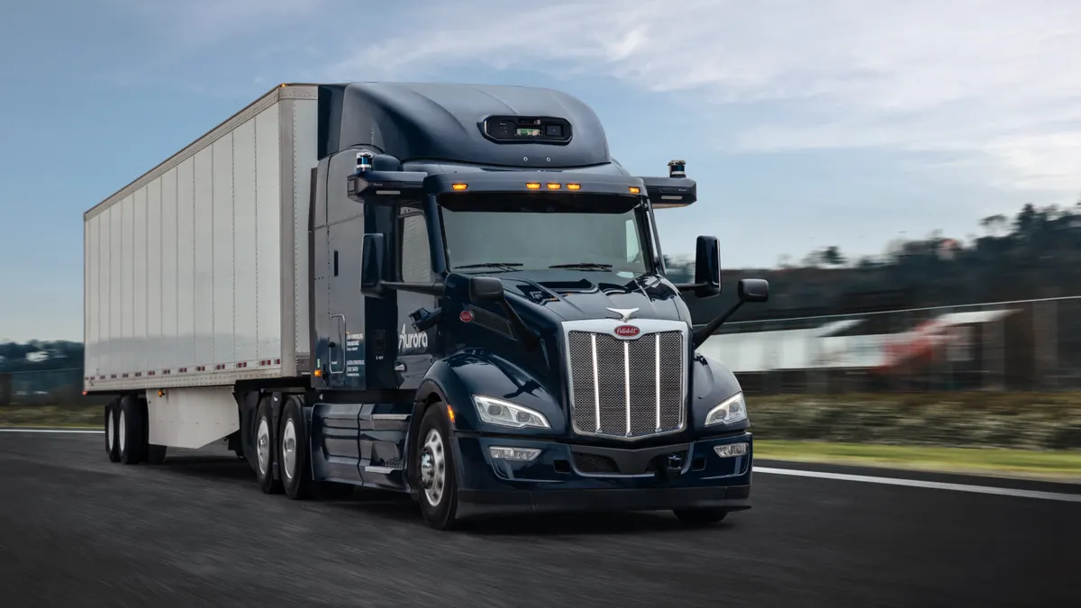 An Aurora driverless tractor-trailer on a roadway with a blurry background.