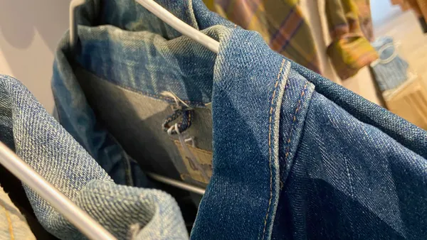 A closeup photo of clothing including jean jackets, hanging on a rack.