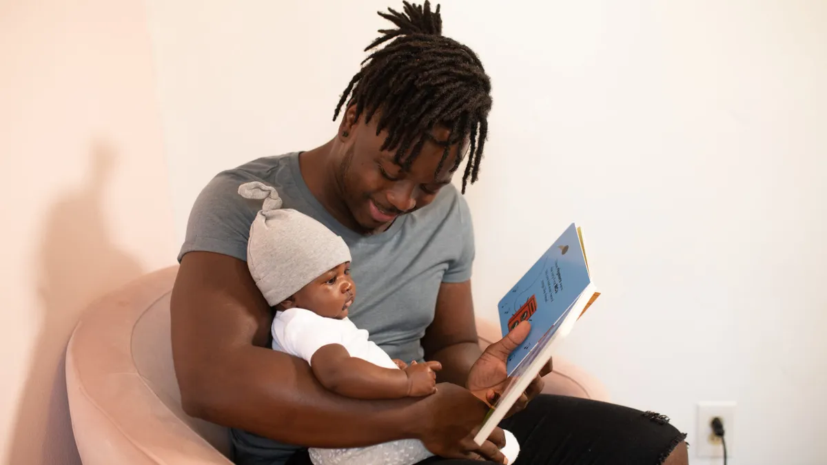 A Black dad reads a book to their baby