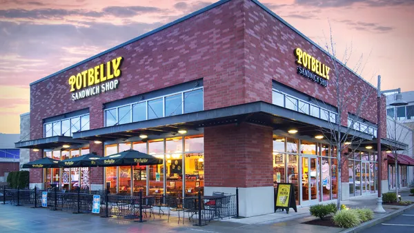 An evening photograph of a brick building with green and yellow signage that says "Potbelly."