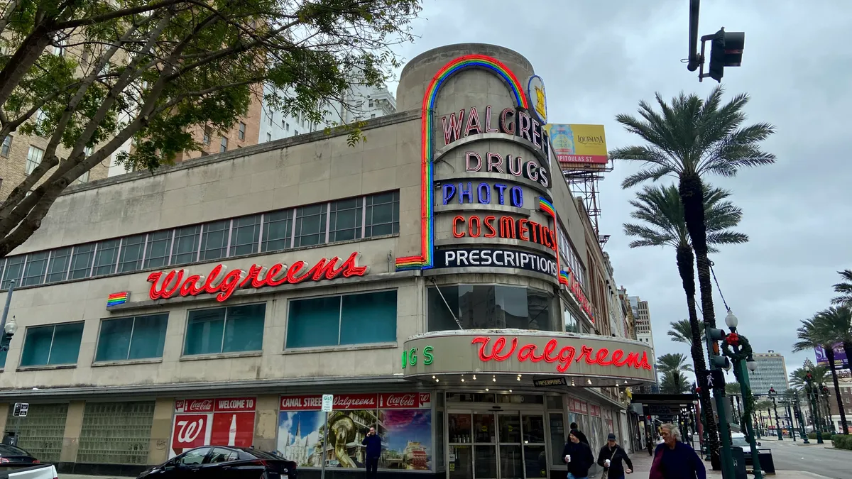 A corner store with lit signage in various colors reads "Walgreens Drugs, photo, cosmetics, prescriptions." Red "Walgreens" signs adorn the sign and a big circular overhang above the corner door.