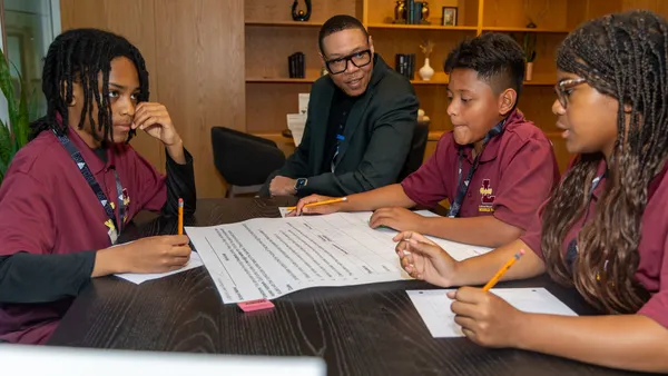 DC Public Schools Chancellor Lewis Ferebee is pictured at a desk between three students during a middle school math competition.