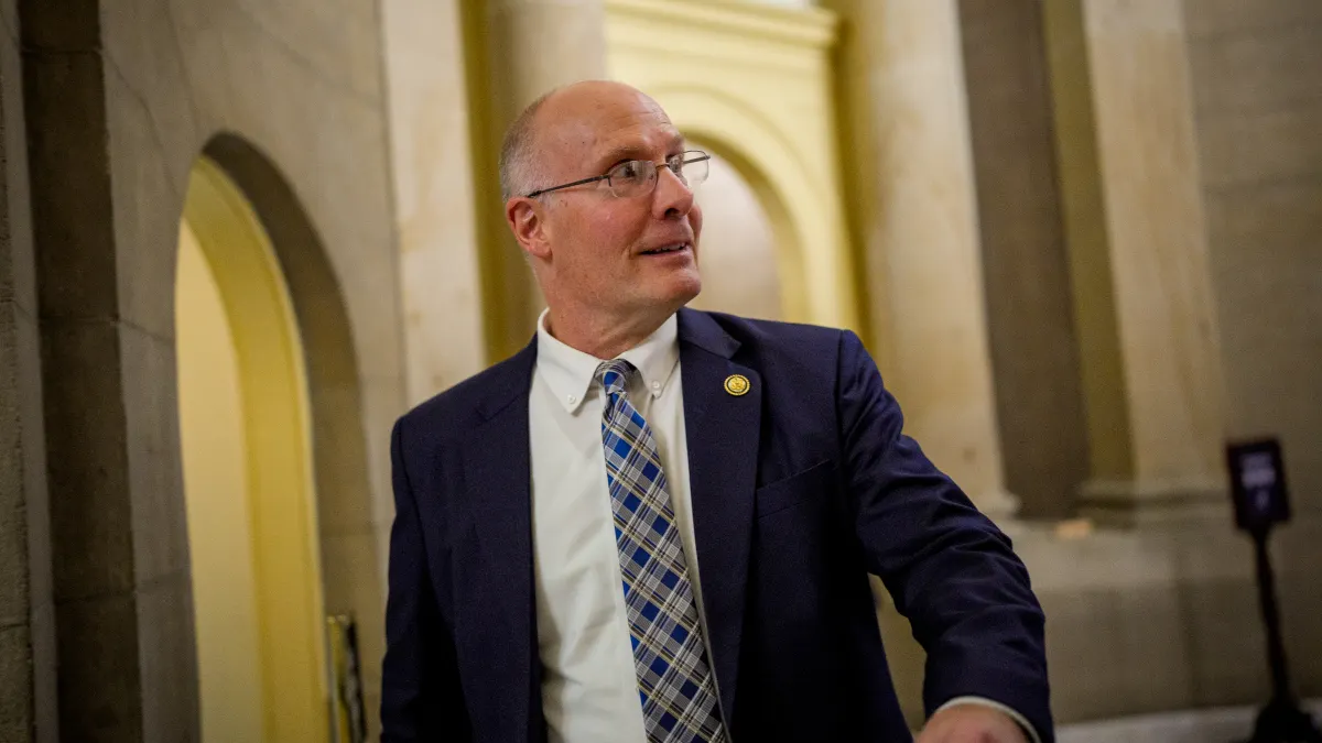 Rep. John Moolenaar sits in a congressional hearing room wearing a dark suit and plaid tie.