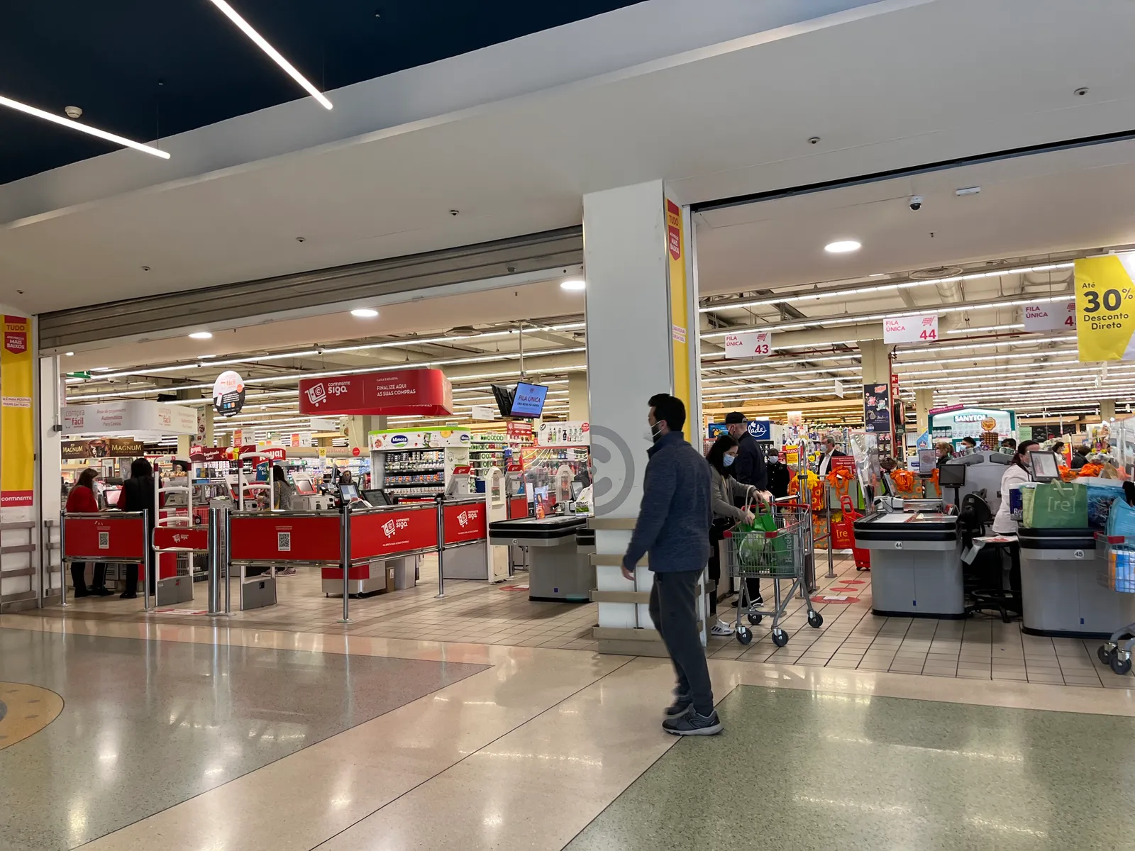 A person walking in front of a grocery store that is inside of a mall.