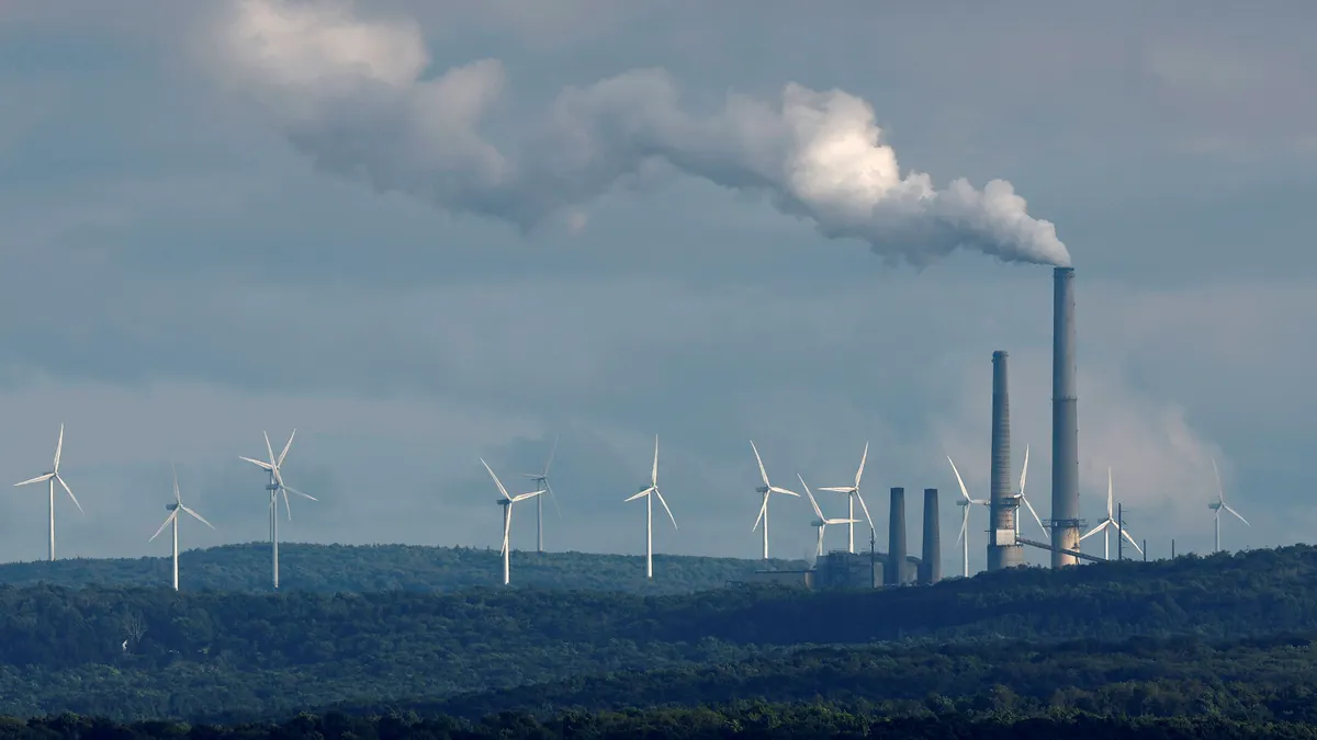 A power plant and wind turbines stand along a hillside.