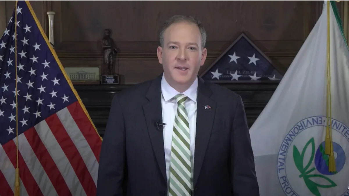 Man standing in a suit in front of a U.S. and EPA flags.