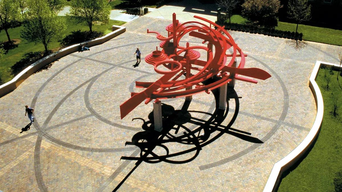 A bird's eye view of a large red metal sculpture on a college campus.