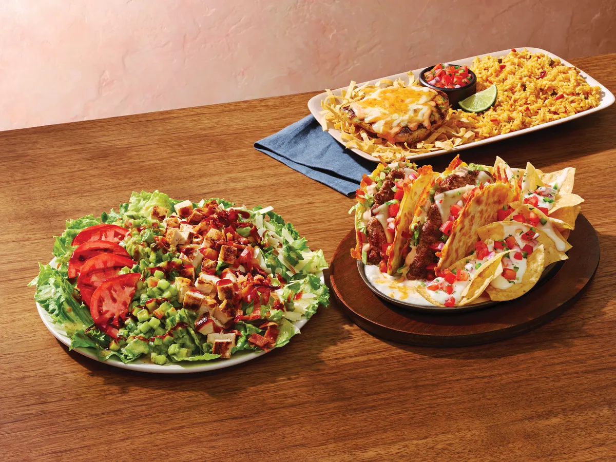 A table with a salad, cheeseburger quesadilla and a plate of rice