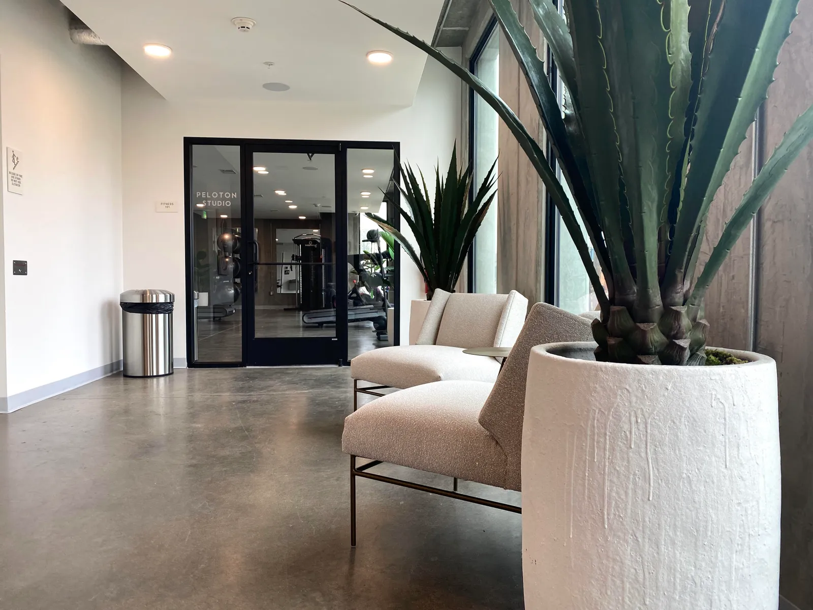 A lounge space with two soft chairs and a mini desk surface next to a room labeled "Peloton Room."