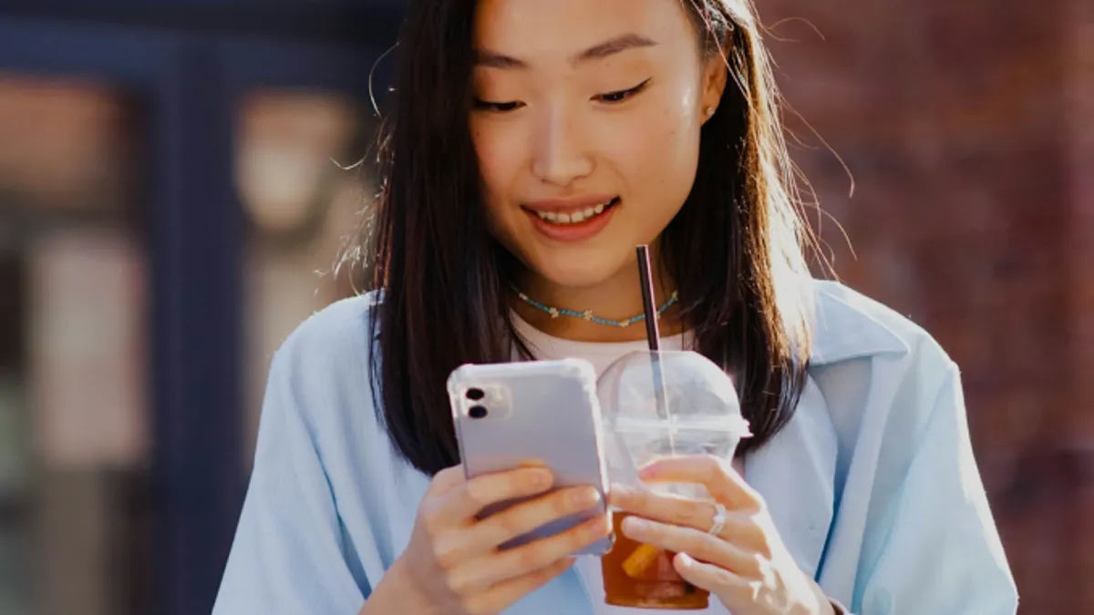 Woman with beverage using smartphone on street