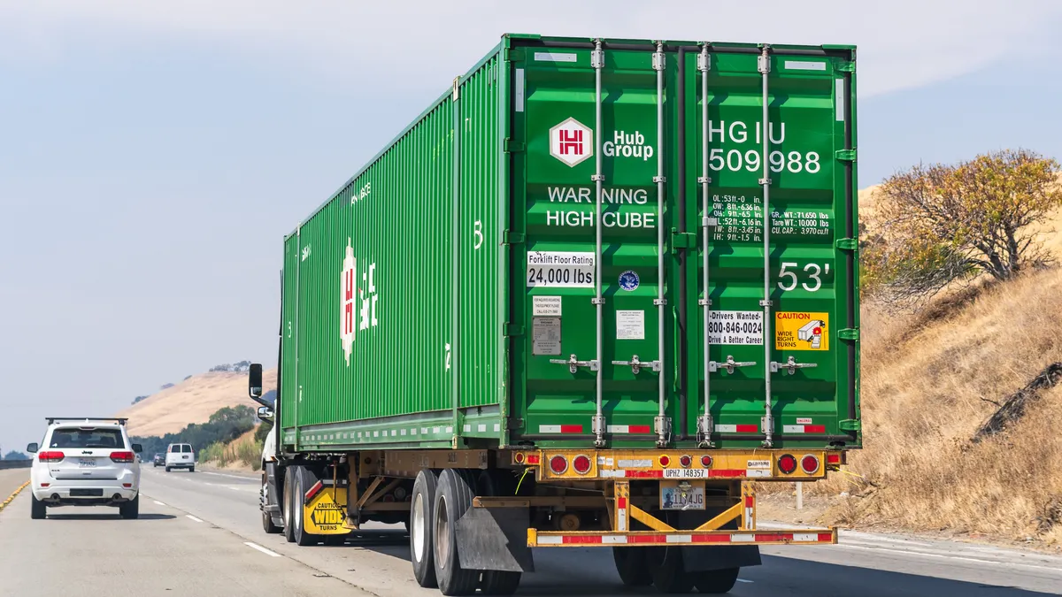 A tractor hauling a Hub Group container on a highway with passenger vehicles nearby.