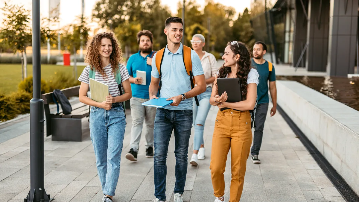 Group of friends walking on the university campus, holding books and notebooks.