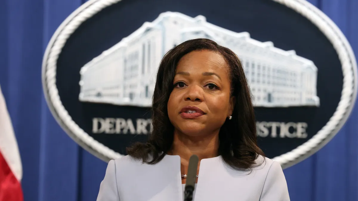 Kristen Clarke speaks at a podium in front of a curtain backdrop and a DOJ logo