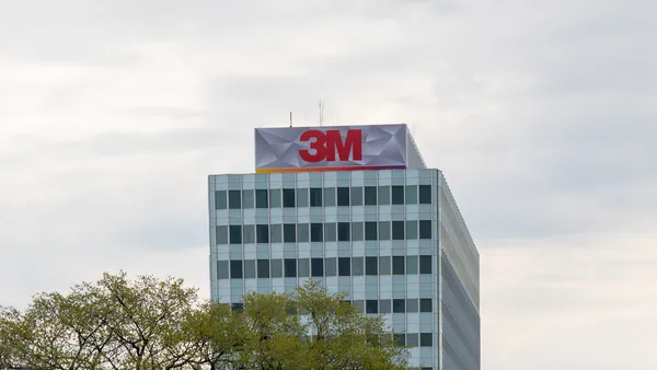 A light-blue and whit building with dark windows and the red 3M sign on top of it on a cloudy day.