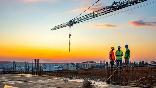 Three construction workers talk under a crane on a jobsite's roof.