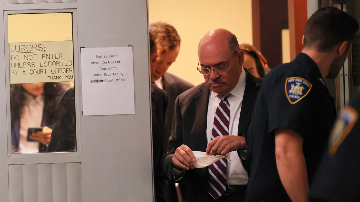 Allen Weisselberg is shown wearing a striped tie, white shirt and dark suit jacket leaving a Manhattan court.